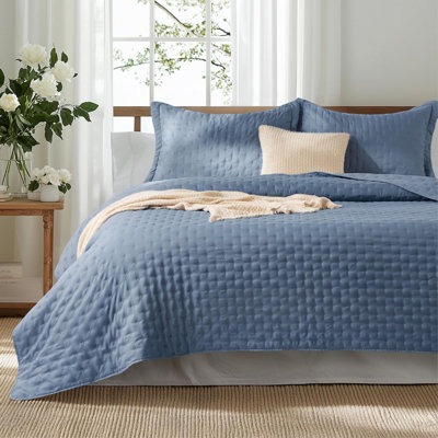 Blue quilt set with embossed square pattern on a bed with matching pillow shams