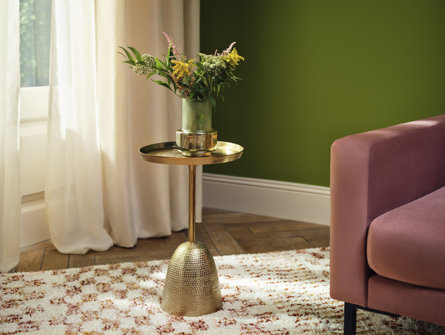 Indoor view of a gold accent table with a green vase and flowers next to a pink chair.