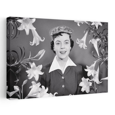 Portrait des années 1950, femme brune souriante portant un bonnet de Pâques regardant la caméra entourée de lys de Pâques