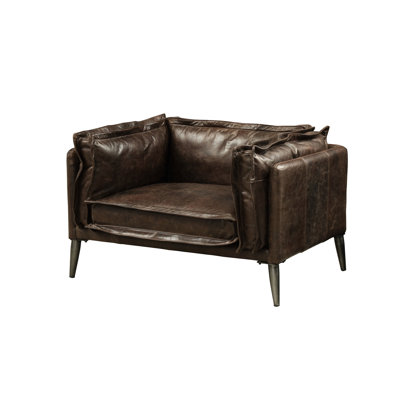 Fauteuil en cuir pleine fleur chocolat vieilli, piètement Kd, dossier fixe et coussin d'assise amovible, assise entièrement en mousse, garnissage en plumes et duvet, coussin carré passepoilé épais, oreiller, accoudoirs enveloppants, pieds en métal de 20 cm.