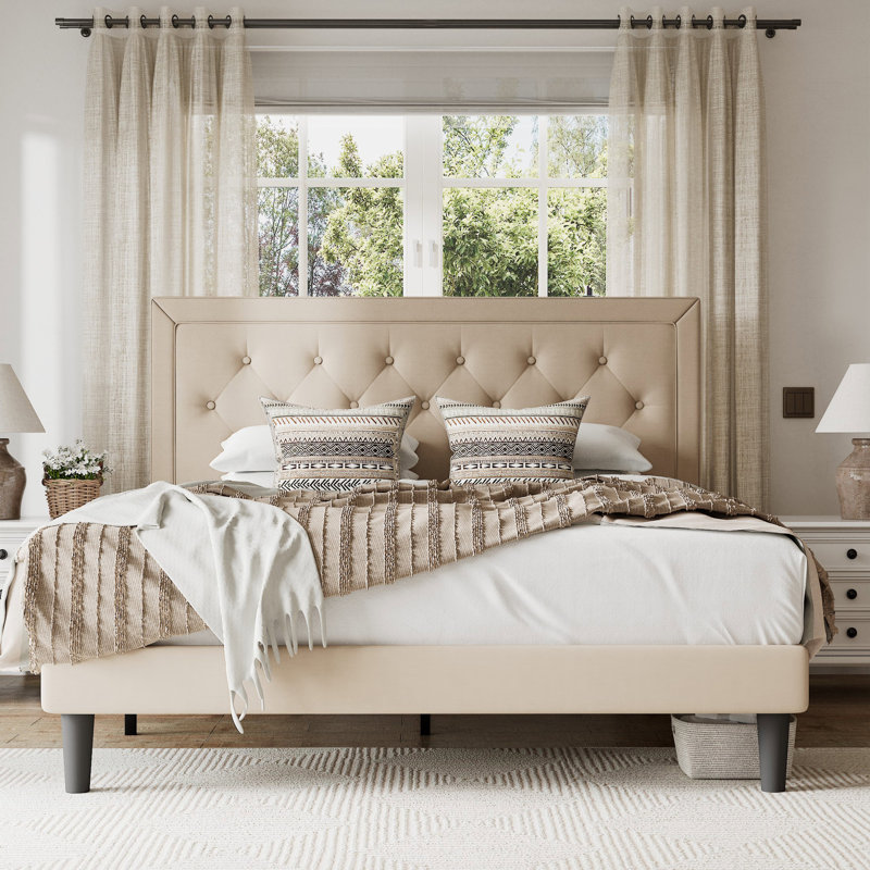 Neutral-colored bedroom with a cream upholstered bed, striped throw blanket, and natural wood nightstands, accented with patterned pillows.