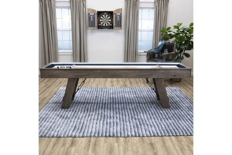 Wood shuffleboard table on a striped blue rug.