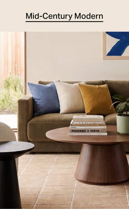 Mid-Century Modern living room featuring a moss green sofa with blue gingham, cream, and mustard pillows behind a walnut wood coffee table topped with stacked art books and a potted plant.