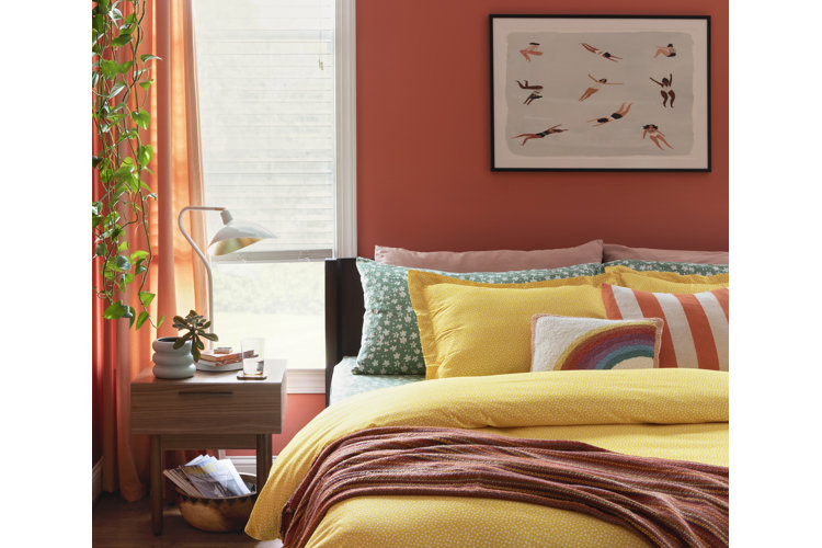 Yellow bedroom idea featuring a bedroom with orange walls and a bed with a yellow comforter and patterned throw pillows..