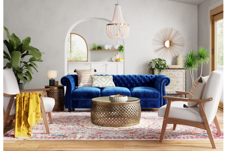a modern bohemian living room with a velvet tufted sofa, wood-frame accent chairs, and gold coffee and end tables