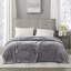 Gray heated plush blanket with two controllers draped over a bed.