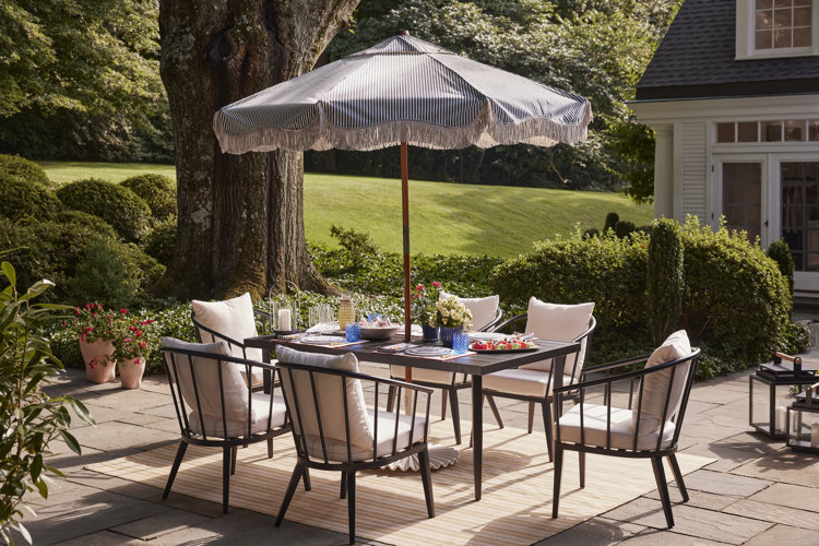 Garden party ideas black wood outdoor dining set on a patio surrounded by shrubs and potted flowers with a striped patio umbrella