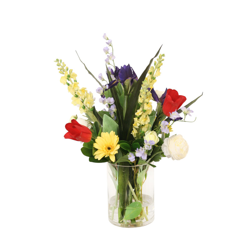 Tulipes rouges mélangées à des mufliers jaunes, iris, renoncules et gerber dans un vase en verre rond