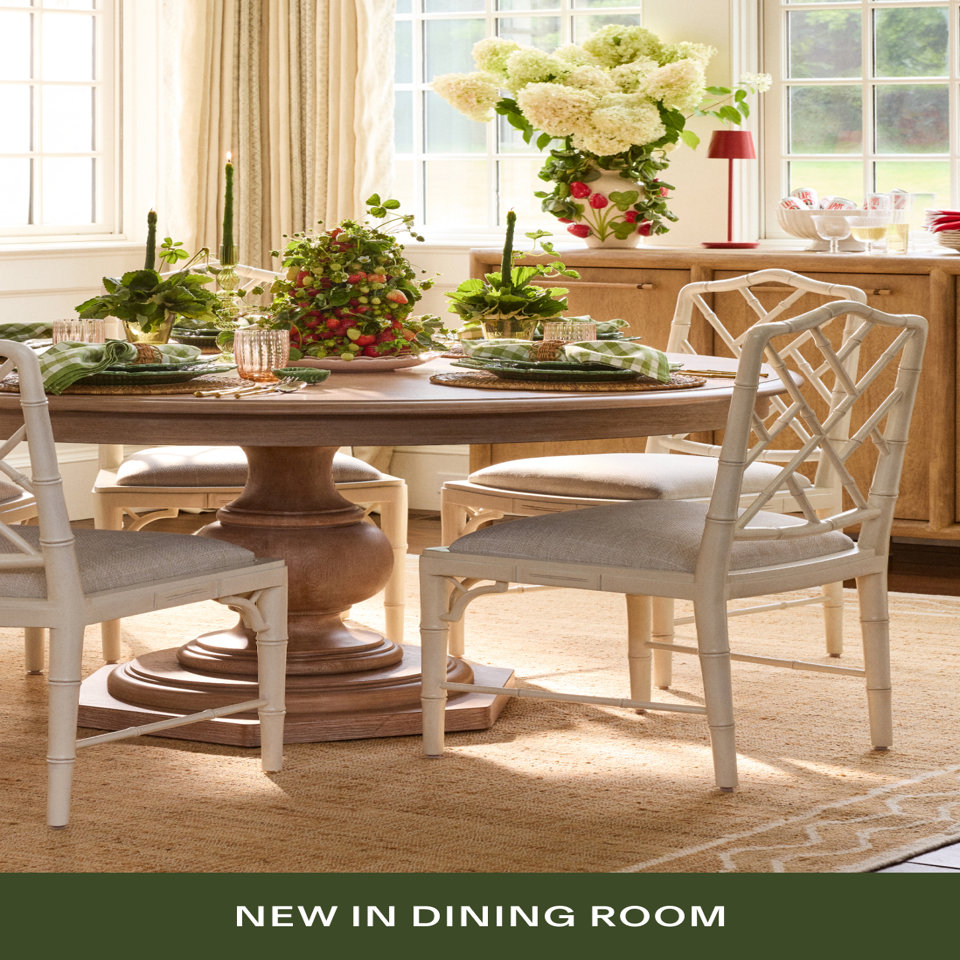 A bright dining room with a round wooden pedestal table, white lattice-back chairs with cushions, a strawberry topiary centerpiece, green tapered candles, and green gingham napkins. Text reads 'NEW IN DINING ROOM'.