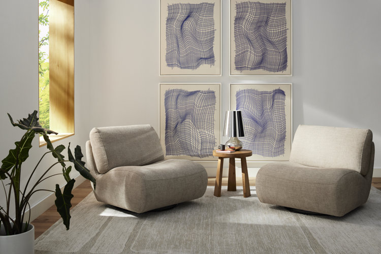 Living room seating area with two modern beige accent chairs a cream and blue gallery wall with four framed pieces of wall art