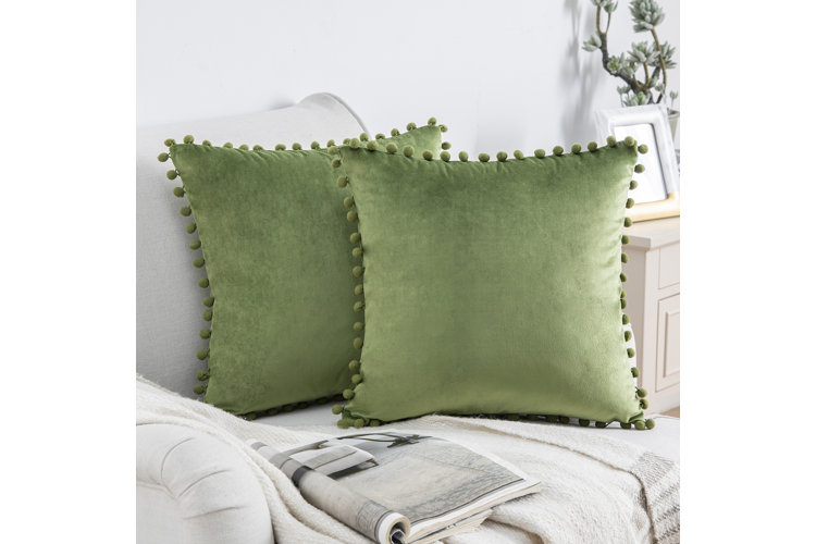 Green decorating idea featuring a pair of green velvet throw pillows lined with mini pom-poms on a white armchair.