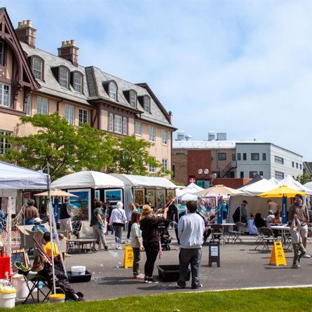 Outdoor arts fair with white tents, artist booths, and visitors enjoying bubble activities on a sunny day