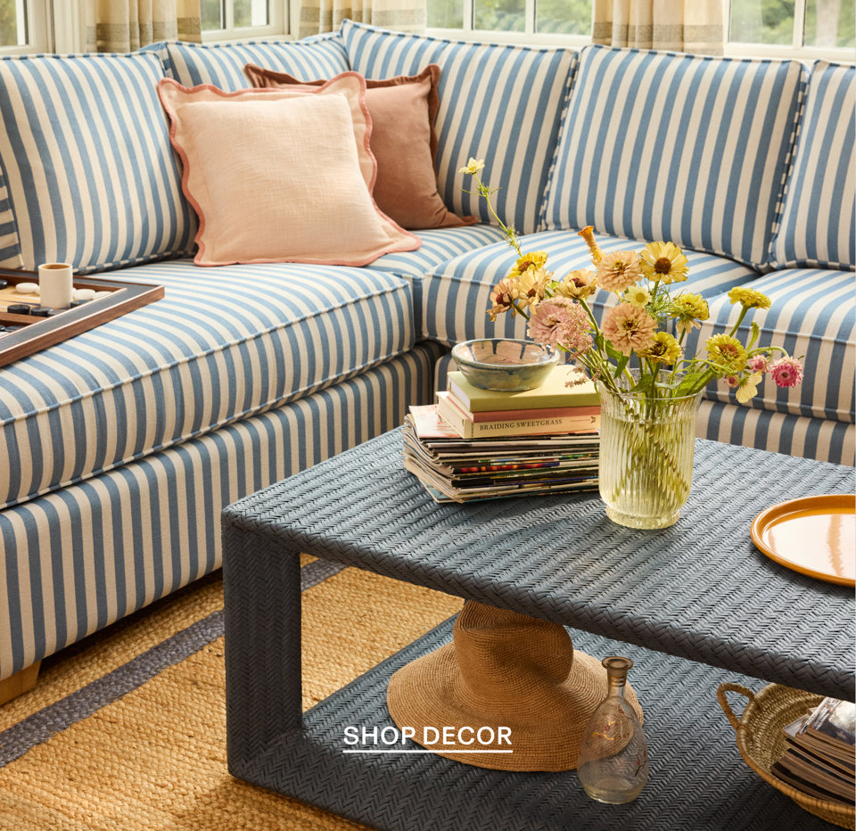 Shop Decor - coastal living room with blue and white striped sofa, pink pillows, wicker coffee table, and fresh flowers
