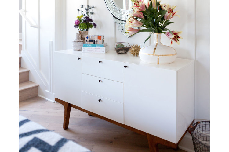 A neutral entryway featuring a minimal white console table with flowers, books, and decorative accessories on top.