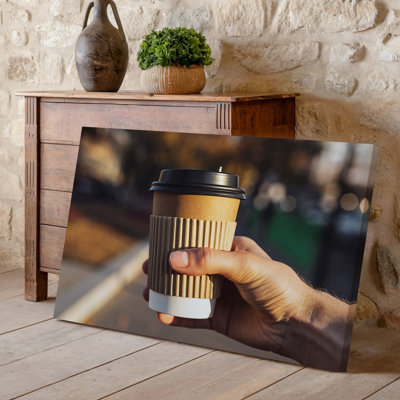 Toile, gros plan d'une main tenant une tasse à café murale jetable avec une pochette en papier brun texturé et une toile noire parfaite pour l'art mural sur toile