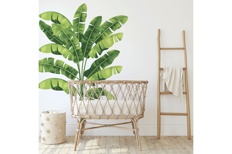 tropical leaf wall decal in a baby nursery with a rattan crib, storage basked, and blanket ladder