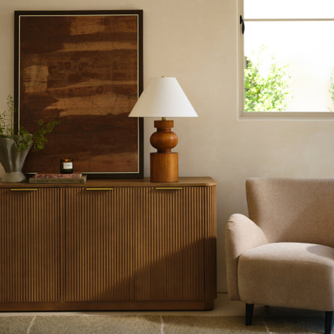Living room with wood cabinet, table lamp, framed painting, and neutral armchair.