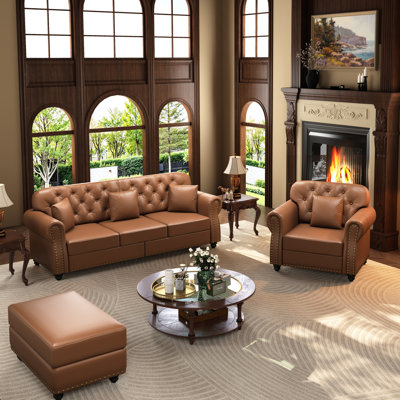 Canapé Chesterfield rembourré en similicuir avec capitonnage à boutons, garniture cloutée, accoudoirs roulés et coussins inclus pour un confort intemporel et une élégance moderne.