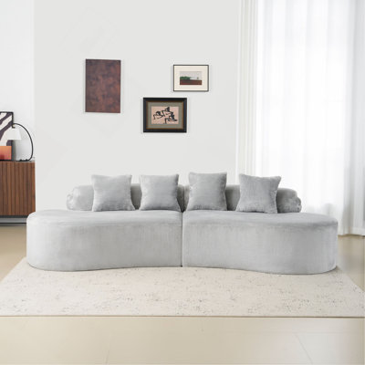 Canapé moderne et épuré en flanelle aux lignes courbes. Canapé d'angle créatif gris pâle pour le salon, avec un assortiment de coussins.