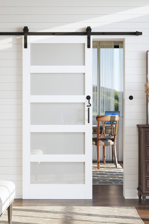 White five-panel sliding barn door with frosted glass inserts and matte black hardware mounted on a white shiplap wall.