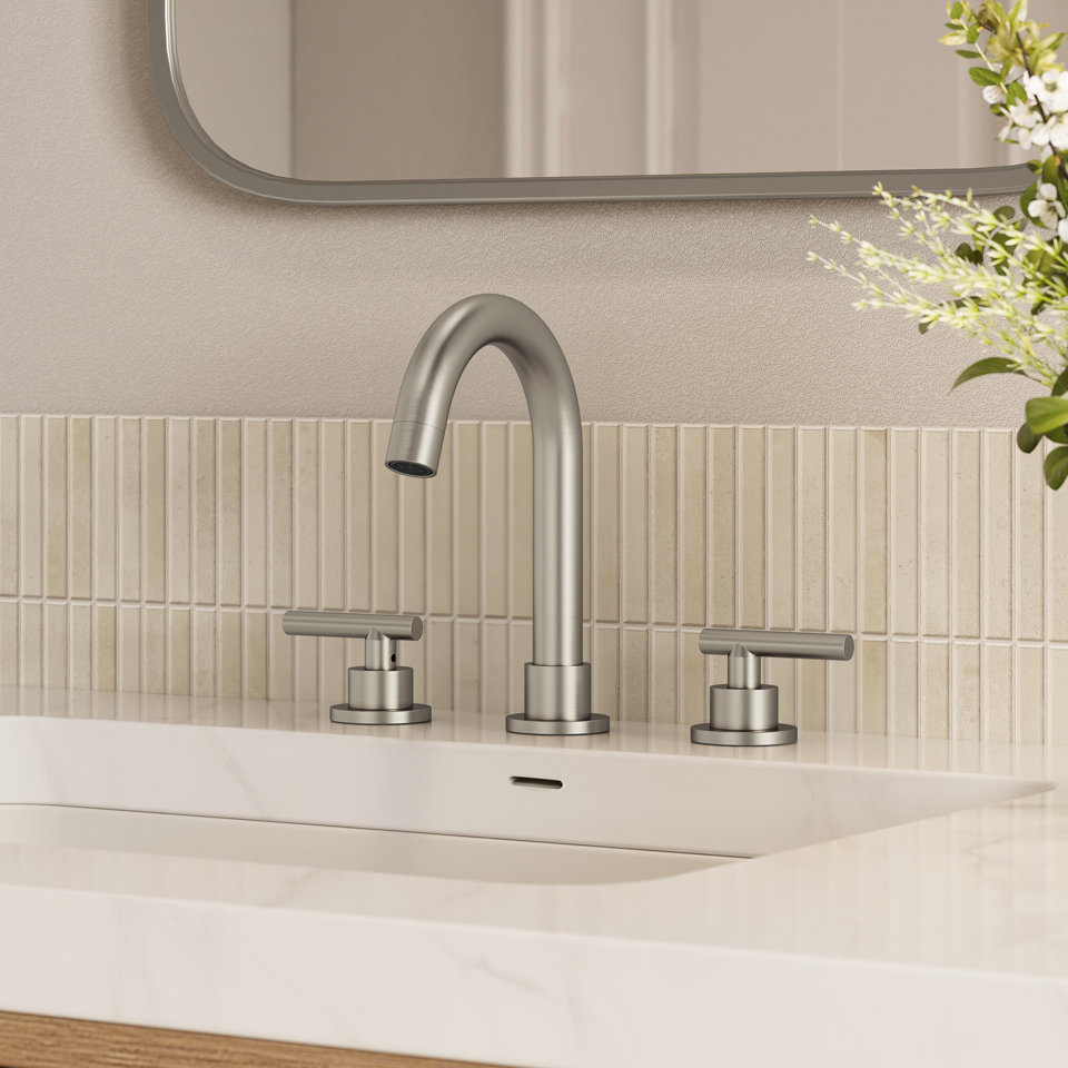 Modern brushed nickel widespread bathroom faucet with two lever handles mounted on a white marble vanity countertop against a vertical tile backsplash.
