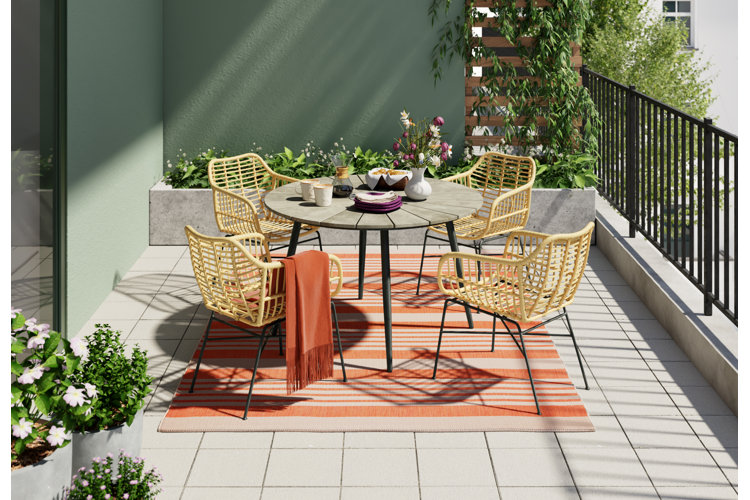 balcony with a striped orange patio rug beneath a wicker rattan outdoor dining set