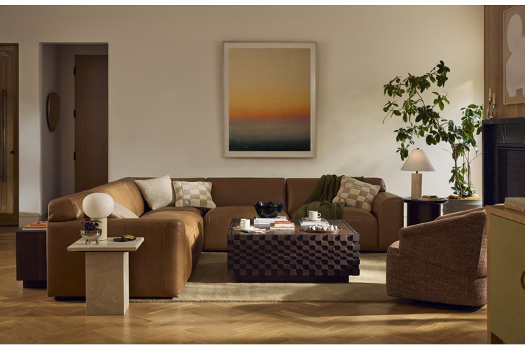 Modern living room with brown leather sectional sofa, wood coffee table, accent chair, and warm neutral decor