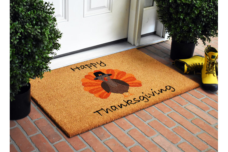 A red brick front stoop with a doormat that has a Happy Thanksgiving quote and an illustration of a turkey with a pilgrim hat.