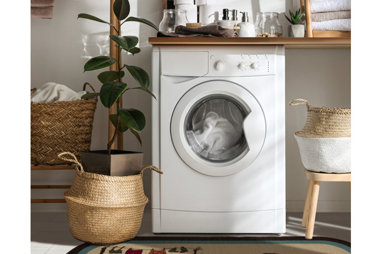A white front-loading washing machine with a load of white towels inside and placed beside wicker laundry baskets.