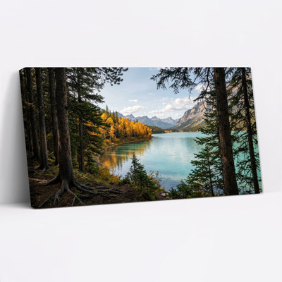 Tableau sur toile représentant des pins encadrant un lac turquoise et des montagnes