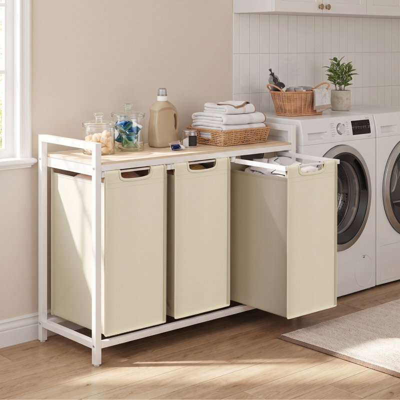Laundry hamper with a white metal frame, wooden top, and three beige fabric pull-out bags.