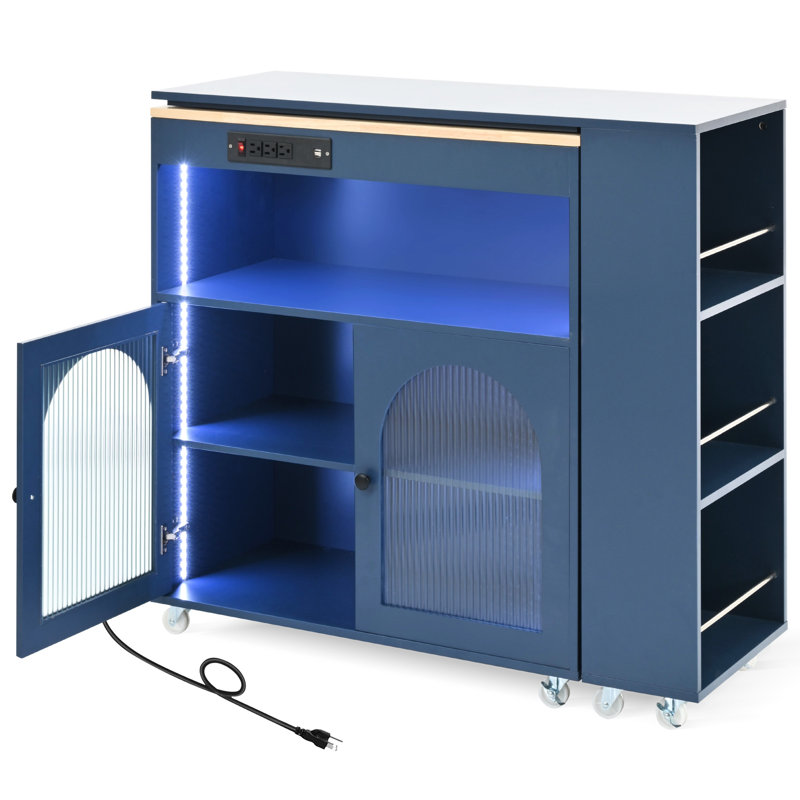 Îlot de cuisine moderne avec rangements, portes en verre cannelé, éclairage DEL, table extensible bleu marine, prise électrique, porte.