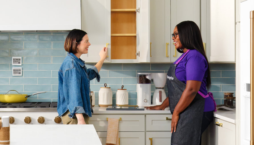 Two people in a kitchen with a Wayfair employee wearing a Wayfair apron.