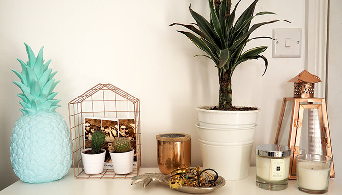 A pastel pineapple, wire and bronze accents, and a plan in a white pot on a shelf