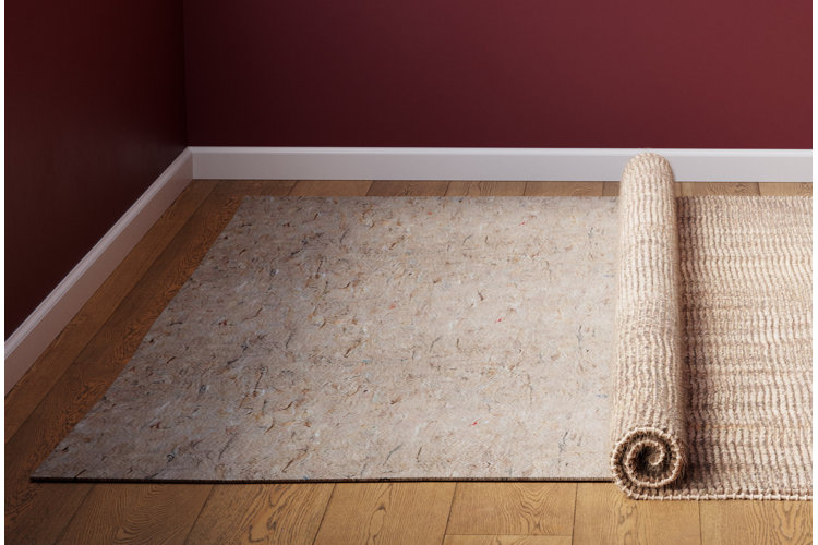 A jute area rug rolled back to show a rug pad on top of hardwood floors.