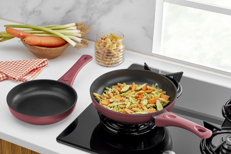 two red skillets one on a stove and one on the counter showing different skillet dimensions
