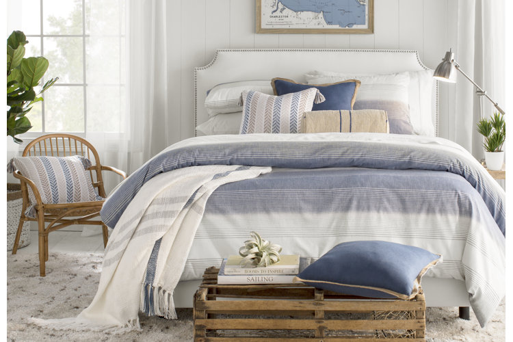 coastal bedroom with blue and white striped bedding and a rattan accent chair