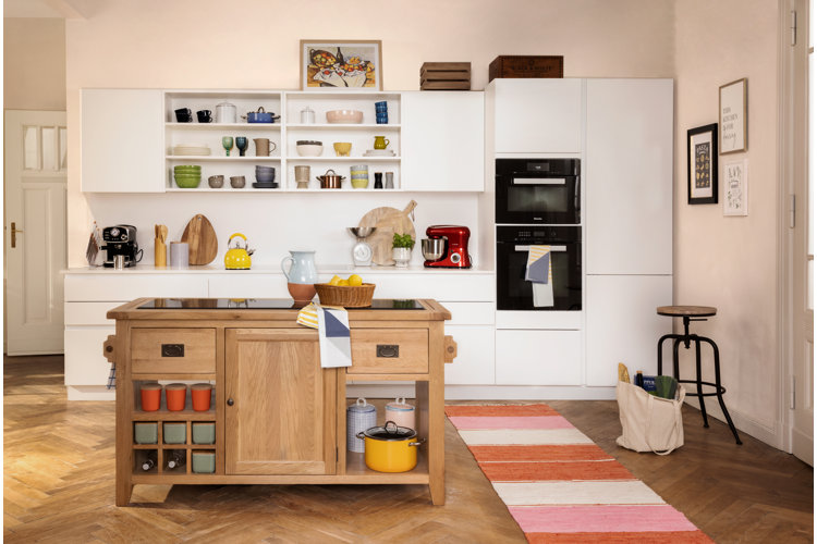 a small kitchen with white cabinets that feature a built-in microwave and wall oven. there is a wood island in the middle of the room.
