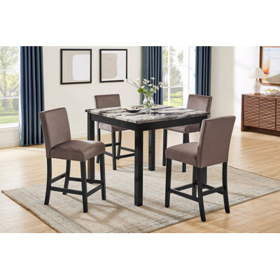 Ensemble de salle à manger avec table haute carrée en imitation marbre, chaises rembourrées en tissu peluche et pieds en bois.