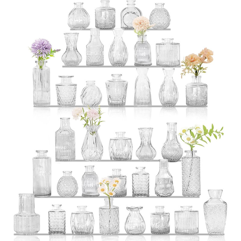 Ensemble de 36 petits vases en verre transparent de forme variée, parfaits pour décorer une table lors d'un mariage champêtre ou pour la décoration intérieure. Ces vases sont composés de bouteilles en verre vintage et sont disponibles en grande quantité. Leurs formes variées en font un choix idéal pour une décoration de table rustique ou pour la décoration de la maison.