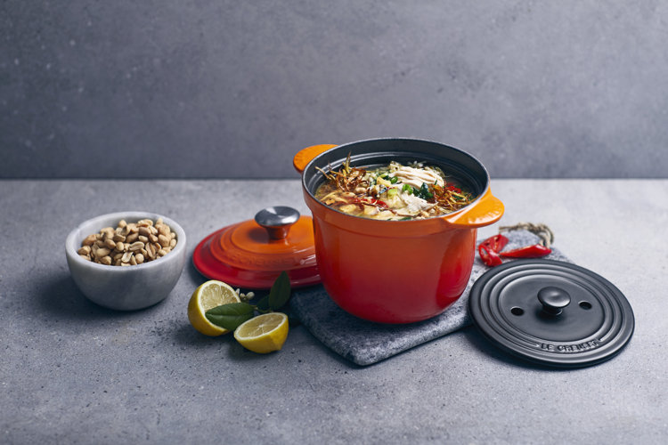 An orange Le Creuset soup pot with ramen in it sitting on a stone trivet