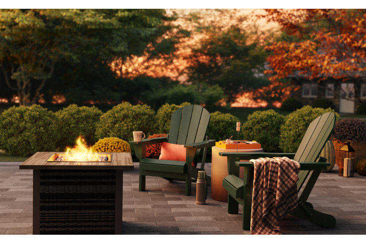 Patio with two dark green adirondack chairs beside a fire pit table and s'mores-making station.
