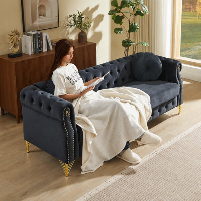 Canapé Chesterfield en velours avec deux coussins ronds, orné de clous en cuivre et de boutons capitonnés, et reposant sur des pieds en métal. Un système d'accroche permet de suspendre des décorations décoratives.