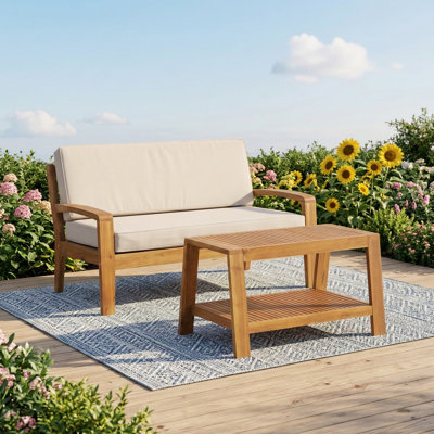 Conversation set crafted from Teak and Acacia wood, including a loveseat and a coffee table. Features beige cushions that resist water. Supports up to 350 pounds. Ideal for patios, decks, and backyards.