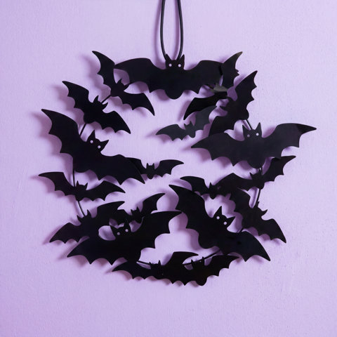 Couronne d'Halloween en forme de chauves-souris noires accrochée à un mur lavande