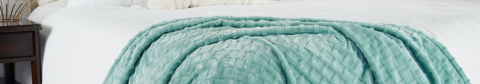 A teal textured throw blanket draped over a white waffle-weave bedspread.