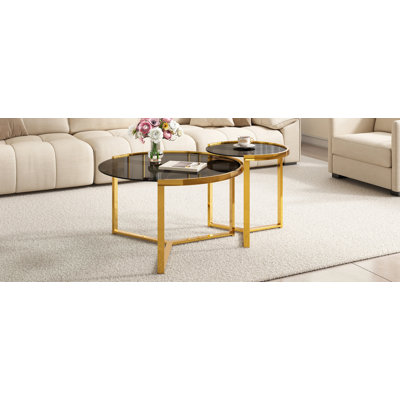 Ensemble de deux tables basses gigognes rondes au style glamour moderne, avec structure en métal doré et plateaux en verre noir.