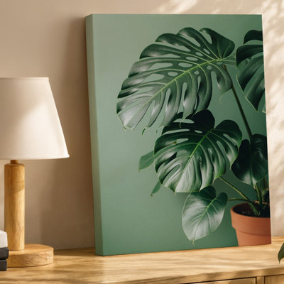 Toile, une plante luxuriante avec de grandes feuilles fendues lustrées est une œuvre d'art bien exposée dans un pot en terre cuite posé sur une toile tendue