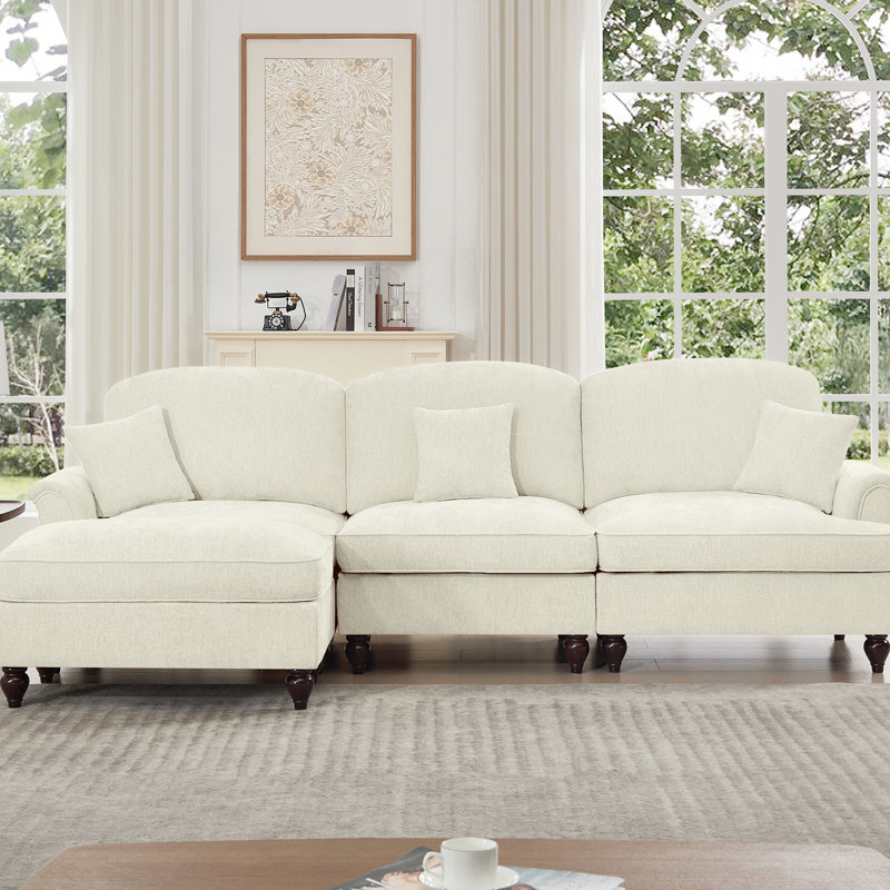 Canapé trois places de style années 50 avec accoudoirs évasés, jupe à volants amovible et plissée, tissu chenille beige et blanc, confortable, modulable et détachable.
