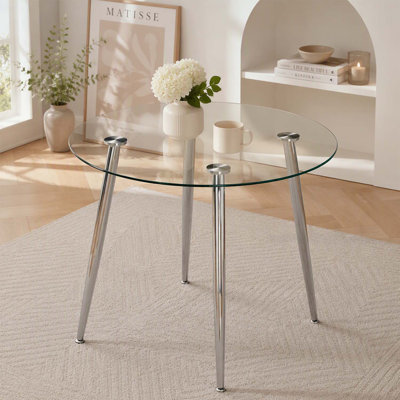 Table de salle à manger ronde moderne avec dessus en verre et pieds argentés, idéale pour des repas élégants et spacieux.